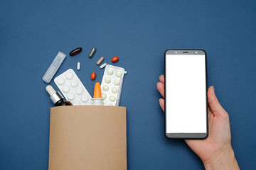 Pharmacy and drugstore online concept. Medicine pills in a paper bag and smartphone on blue background, space for text