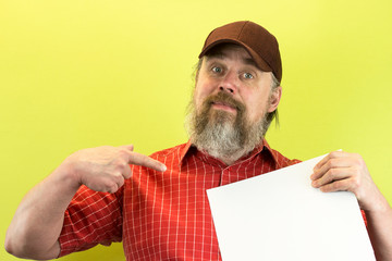 Male construction worker holding blank advertising board. Construction worker with poster. A rude, bearded, stern man in a red shirt and a baseball cap shows a message