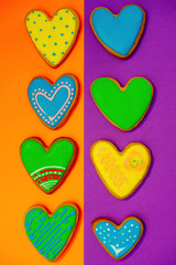 Sweet holiday cakes in the form of hearts covered with colored glaze with handmade patterns on bright backgrounds.