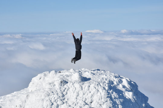 Happy mountaineer jump into the air on the top of the mountain. Climber celebrate success jump with hands up high above the clouds
