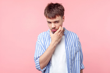 Portrait of pensive brown-haired man with small beard and mustache in casual shirt touching his...