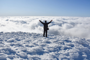 Happy mountaineer raise hand up on top of mountain. Climber enjoy on snowy mountain high above the clouds