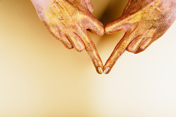 Female hand in golden glitter showing heart shape