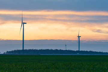 germany: wind turbines, windmills in the sunset, green grassland, yellow orange sky with clouds