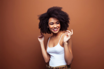 pretty young african american woman with curly hair posing cheerful gesturing on brown background,...