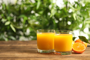 Glasses of fresh tangerine juice and fruits on wooden table