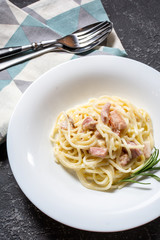 Pasta carbonara served on deep plate decorated with rosemary.