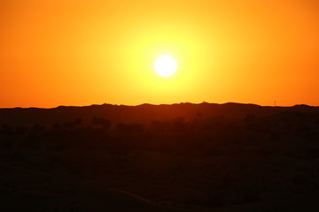 Orange sunset in the desert with silhouette of mountains