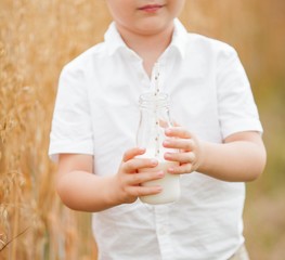 Close-up. Portrait of a boy in a wheat field. A boy drinks milk from a glass bottle.