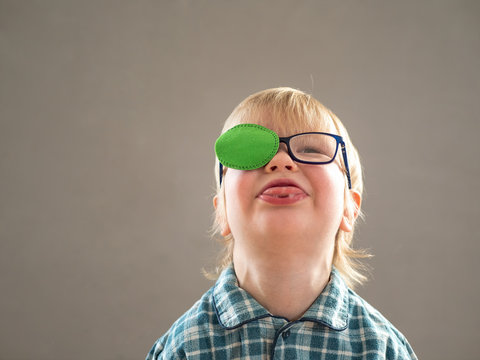 Portrait of funny child in new glasses with green spot to correct strabismus.Orthopedic Boys Eye Patches nozzle for glasses for treatment of strabismus (lazy eye). Boy puts on and corrects glasses