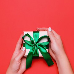 Woman presenting gift with green ribbon on lush lava color background, copyspace. Valentine's Day or Mother's Day greeting card in trendy colors, top view