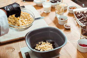 cropped view of chocolatier adding white chocolate chips into bowl on kitchen scales