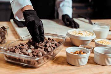 cropped view of chocolatier in black latex gloves taking dark chocolate cubes