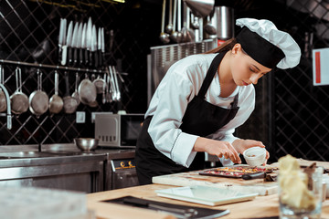 selective focus of attractive chocolatier in apron looking at dark chocolate bars