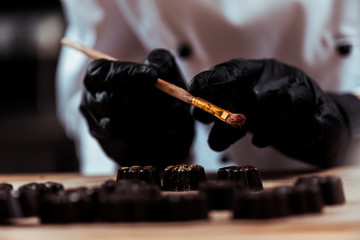 cropped view of chocolatier holding brush near chocolate candies