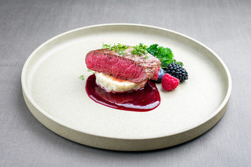 Fried dry aged venison tenderloin fillet medallion steak natural with mashed potatoes and raspberry sauce as closeup on a modern design plate