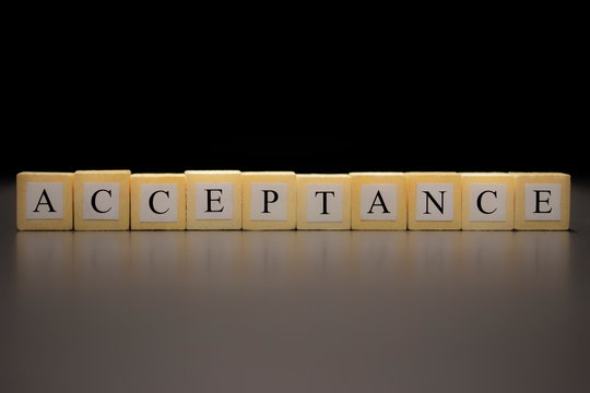 The word ACCEPTANCE written on wooden cubes isolated on a black background...
