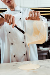 cropped view of chocolatier pouring melted white chocolate on marble surface
