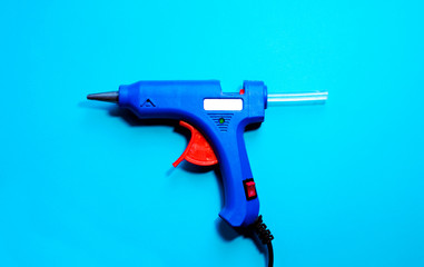 Electric blue hot glue gun with glue stick on a blue background