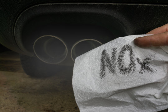 Hand holding a dirty white cloth in front of the smoking exhaust of a car with diesel engine.