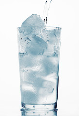pouring water in a glass full of ice cubes, white background, blue toned object