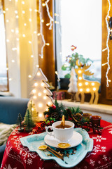 Herbal tea with white cup. At background there are Christmas tree and deer with light. Cozy Christmas Background with healthy herbal tea.