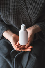 White cosmetic bottle in a female hands. Vertical mock-up.