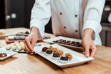 cropped view of chocolatier touching plate with sweet fresh chocolate candies