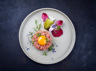 Gourmet tartar raw from beef fillet with yellow of the egg and vegetable as top view on modern design plate