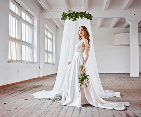 Beautiful bride in a wedding dress in a bright stylish Studio. Wedding in European style. Decor and bouquet in hand.