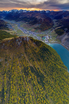 Sunset over larch woods on Crap de La Pare ridge towards Livigno village and lake, aerial view, Valtellina, Lombardy