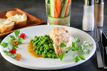 White festive dish with fried chicken breast and broiled green beans on the dark background. White cut bread and thin slices of cucumber and carrot in a glass.