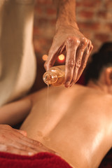 Alternative Medicine. Therapist healing woman doing abhyanga back massage pouring herbal oil on skin close-up