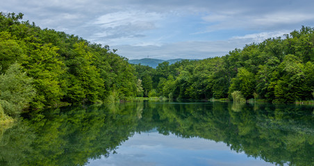Fototapeta na wymiar Panorama of a lake in Maksimir park with green tree reflections and a mountain Medvednica in Zagreb