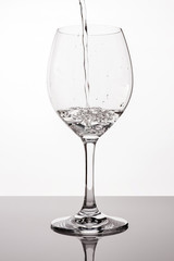 Pour water into clear glass. Drinking water pouring in wine glass. Splash of water in glass on white background with bubbles. Studio shot. Water is the basis of life. Concept of a healthy lifestyle. W