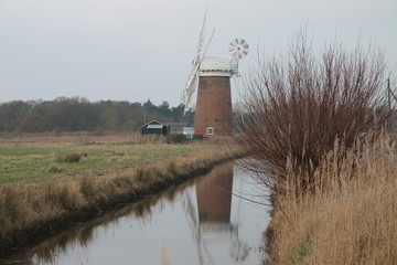 Beautiful rural landscape windmill brick building old brick vintage building Horsey Pump with wooden white sails on Norfolk Broad water canal flat en land East Anglia England cold pink sky reflected