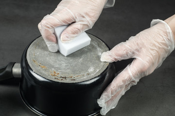 Hands in gloves cleaning old pot with eco friendly magic sponge, no detergent house cleaning