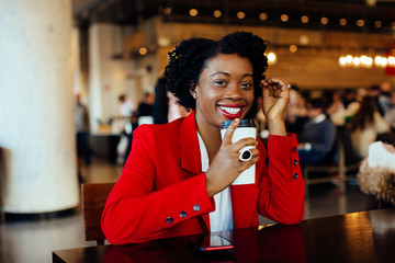 Portrait of a smiling, happy young woman sitting in a cafe holding paper coffee cup with plastic lid