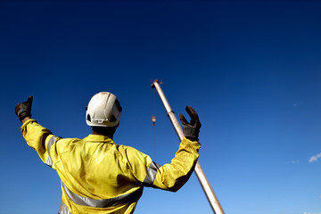 Rigger wearing a glove standing raising using a hand signal by moving finger slowly to direct communication with crane driver to move the boom up at construction site, Sydney, Australia   