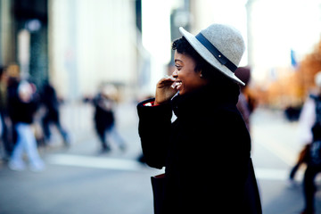 Portrait of a happy smiling woman in faux fur coat and leather bag crossing a busy urban street