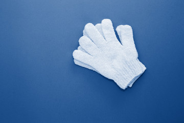 Woman exfoliating massage glove on blue background.Gloves for use in shower for massage and scrub. Beauty background with cosmetic products toned trendy classic blue color of the year 2020. 