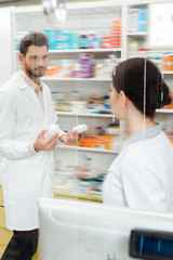 Obraz premium Selective focus of pharmacist with pills looking at colleague at drugstore counter
