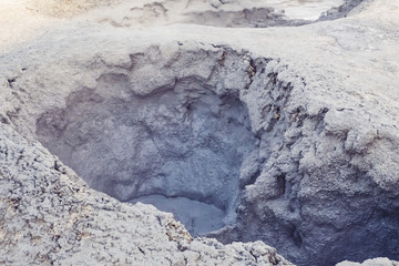 Mudpots in the geothermal area Hverir, Iceland. The area around the boiling mud is multicolored and cracked.