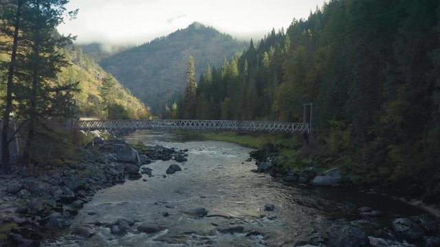 Aerial: Old footbridge crossing the Lochsa river in a forest.  Nez Perce Clearwater National Forests, Idaho, USA. 6 October 2019