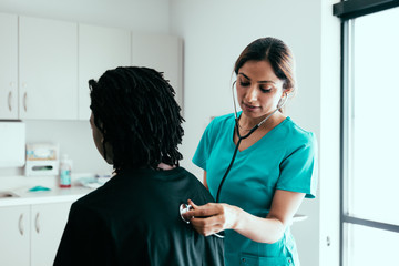 Female patient sitting while nurse holds stethoscope to chest