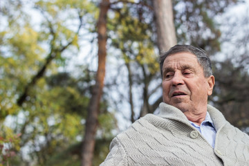 Naklejka na ściany i meble Portrait of happy senior man smiling, in the public park, outdoors. Old man relaxing outdoors and looking away. Portrait of elderly man enjoying retirement