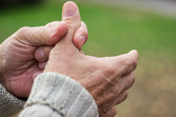 Elderly man has pain in fingers and hands. Old man with finger pain, bokeh background, outdoors