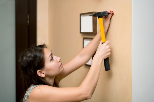 Girl hammer a nail into the wall to hang a photo frame