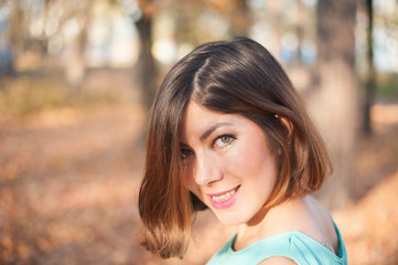 Fototapeta premium pretty dark-haired girl in blue smiles, looks over her shoulder in the park in autumn