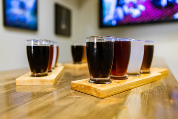 Flight of craft four of different beers glasses on wooden trays during a tasting session, selective focus with blurred bar background and copy space